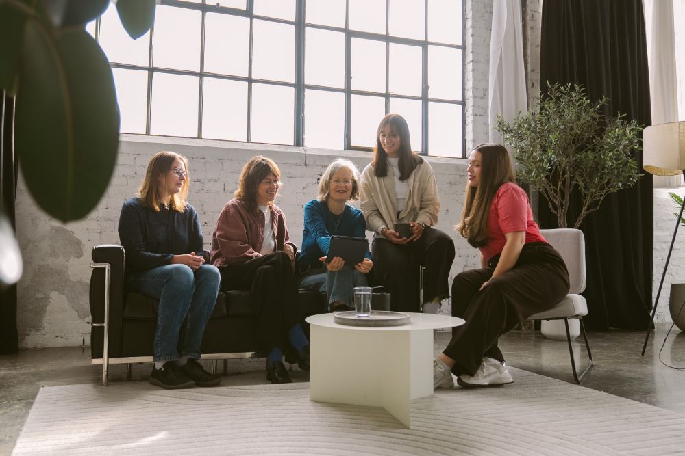 Fünf Frauen sitzen und stehen in einem modernen Raum zusammen